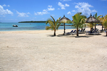 Thatched parasols and sun loungers at a beautiful beach with white sand in Mauritius - a motorboat anchoring in the lagoon