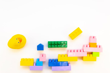 Top view mess made of colorful plastic building blocks and rubber yellow duck on white