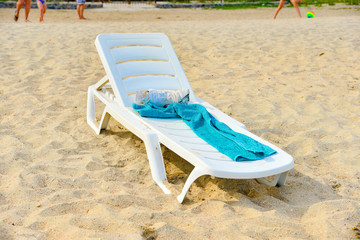 An empty deck chair with a towel stands on the beach by the sea.