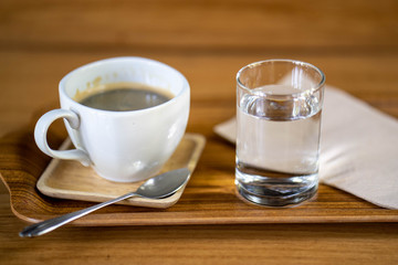 Cup coffee, glass water on wooden tray.