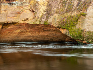 a landscape with a steep river and caves on a sandstone cliff