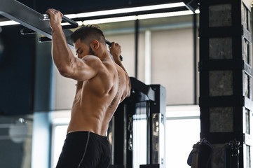 Fototapeta na wymiar Muscular athlete pulling up on horizontal bar at gym