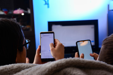 friendship, people, technology and entertainment concept - A mother and son holds a smartphones in theirs hands using a DLNA in the living room in front of the TV, enjoying numerous content over 