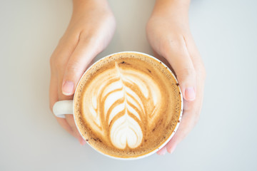 Woman hand holding a white coffee mug.  Coffee is a latte. table on the wooden table in vintage style, taken from the top view, see the froth of milk foam.