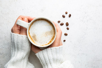 Cup of coffee in womens hand on white background, top view