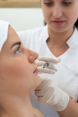 Powiększenie ust kwasem hialuronowym. Twarz kobiety podczas zabiegu modelowania ust. Kosmetolog wstrzykuje wypełniacz, medycyna estetyczna.  - obrazy, fototapety, plakaty