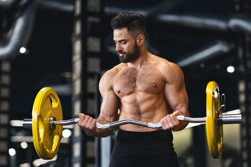 Fototapeta na wymiar Muscular bodybuilder training arms with barbell in gym