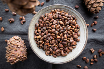 Cedar or pine nuts in a bowl with cones on gray background, top view