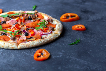 A fresh prepared pizza with salami, mushrooms, ham and cheese on a dark background. Italian traditional lunch or dinner. Fast food and street food concept. Flat ly, top view, copy space fot text