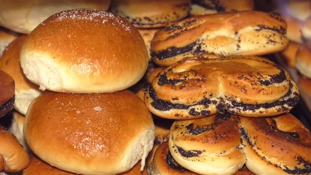 fresh lot of baked buns on counter, illuminated by the sun. Assortment of sweet pastries on the cafe counter, bread roll with poppy seeds, cinnamon.