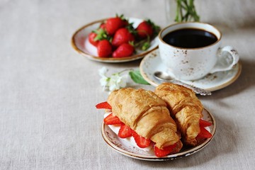 Breakfast in French. Croissant sandwich with I soft cheese and strawberries. And black coffee, a bouquet of flowers. Fresh strawberries. Soft focus. Space for text.  Copy Space
