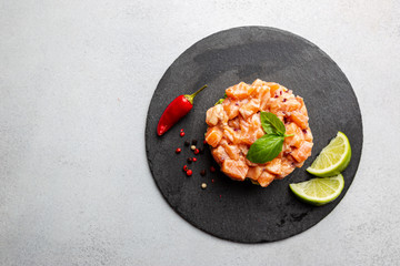 Delicious avocado and raw salmon salad, tartare, served on a black plate with lime, light background, top view