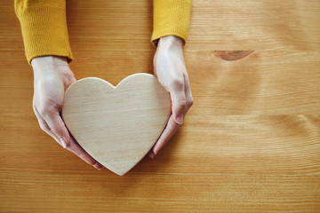Valentine's day. Wooden heart in the hands of a girl on the table