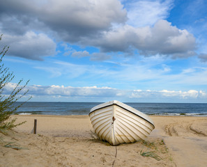 Lonely boat lying on the sand beach at the coast of the island usedom, Germany, under a blue and cloudy sky.