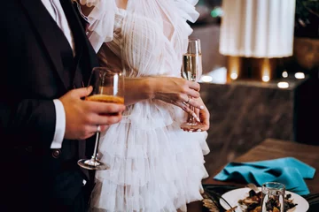 Midsection of bride and groom holding glasses of wide at wedding party © kavoons