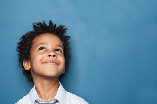 Little black child boy smiling and looking up on blue background