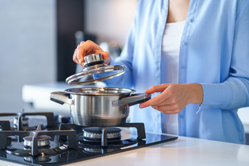 Woman housewife using steel metallic saucepan for preparing dinner in the kitchen at home....