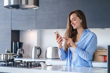 Young happy woman using smartphone and wireless headphones for listening music and making video...