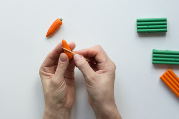 Woman hands making strips with tooth stick on orange carrot from polymer clay