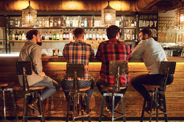 Rear view friends sitting on chairs talking at the bar in a bar. - obrazy, fototapety, plakaty