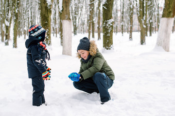 Fototapeta na wymiar Older brother teaches to make snowballs younger brother. Happy family vacation. Kids playing with snow