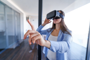 Amazed surprised young woman with virtual reality glasses touching the air during the VR experience at home