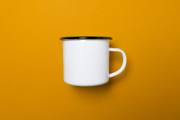 Emaille Tasse auf gelben Hintergrund freigestellt seitlich im Profil mit leichten Schatten