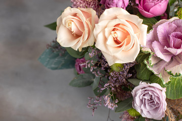 bright bouquet of different varieties of roses with a rosette of brassica on a gray background. horizontal image, copy space