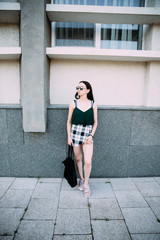 Obraz premium Sexy girl in a T-shirt, sunglasses and mini shorts near the wall