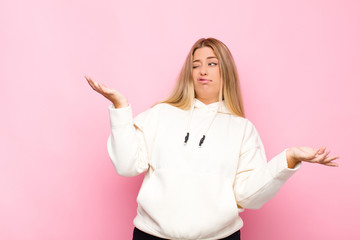 young blonde woman shrugging with a dumb, crazy, confused, puzzled expression, feeling annoyed and...
