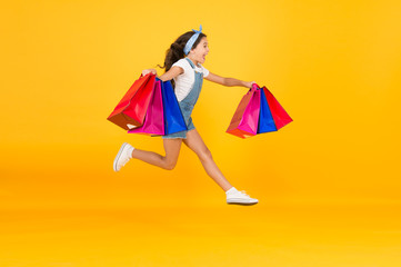 Trends and brands. Towards discounts. Happy girl jump with shopping bags. Little child smile with...