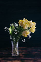 Yellow tulips in a vase on a wooden background