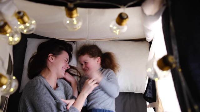 Top View On Affectionate Happy  Mom And Cute Small Child Daughter Tickling Laughing Having Fun Lying On Tent And Playing, Young Mother Foster Parent Hug Small Kid Girl Cuddling Touching 