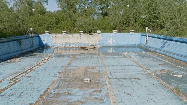 Drone dolly shot of an abandoned, derelict swimming pool at the desolated holiday resort. Urban exploration or urbex video.