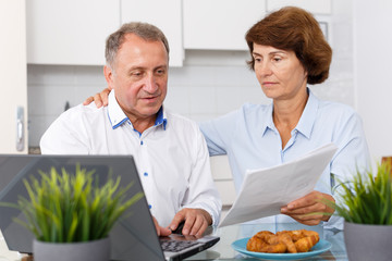 Mature man and woman with documents talking while working at laptop