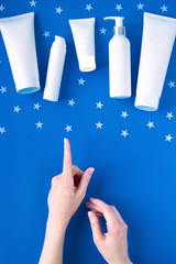 White empty cosmetic tubes and female hand on blue background. Concept night skin care, choice of cosmetics. With copy space. Flat lay. Top view.