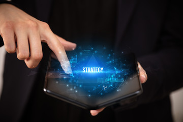 Businessman holding a foldable smartphone with STRATEGY inscription, business concept