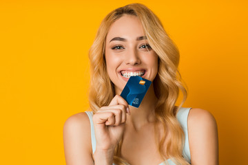 Playful girl biting credit card, thinking of doing online shopping