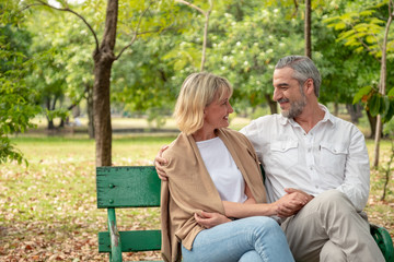 Happy elder Caucasian couple sitting at bench and holding hand each other in park. Happy elder couple concept