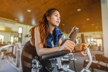 Naklejka na ściany i meble fitness ,workout, gym exercise ,lifestyle and healthy concept. Front view of woman workout with bike. Women exercise working out in the gym for healthy lifestyle on bike at sunset.