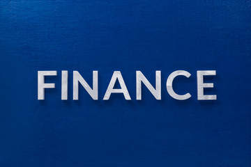the word finance laid with silver metal letters on classic blue board in flat lay with central...