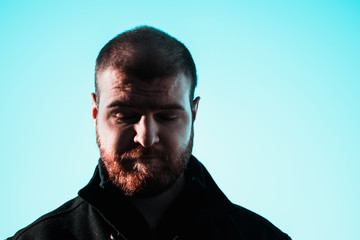 Sad depressed face of a short haired balding bearded man looking down at the floor. Eyes closed in defeat. Dark harsh shadows on mans face