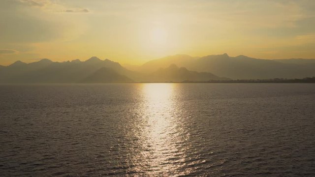 Colorful magic golden panorama of sunset goden sea water, cloudy sky and silhouettes of mountains. Beautiful outdoor amazing scene of dramatic landscape of Turkey in Antalya. Real time 4k video.