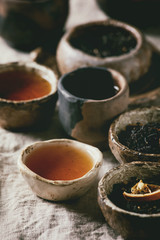 Variety of hot and dry tea green and black in traditional and wabi sabi style fireclay ceramic craft cups and bowls, served on linen cloth as background. Close up