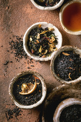 Variety of hot and dry tea green and black in traditional and wabi sabi style fireclay ceramic craft cups and bowls, served on clay board as background. Flat lay, space