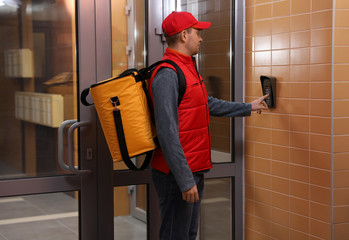 Male courier with thermo bag pushing intercom button. Food delivery service