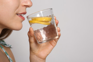 Young woman drinking lemon water on light background, closeup