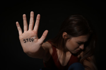 Crying young woman showing palm with word STOP against black background, focus on hand. Domestic...