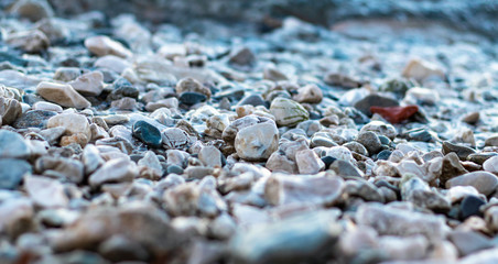 Gravel pebbles at the beach shore, cold photo. Wet stones reflecting sunlight , many different colors of round pebbles