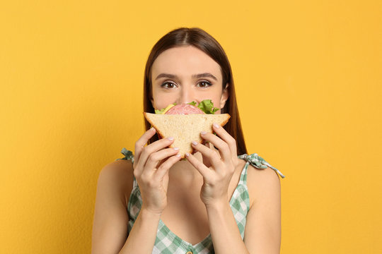 Young Woman Eating Tasty Sandwich On Yellow Background